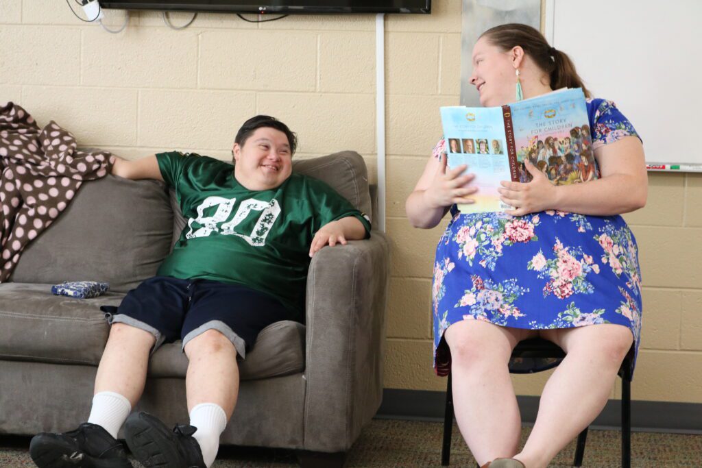 a person sitting on a couch next to a person sitting on a chair and holding a book