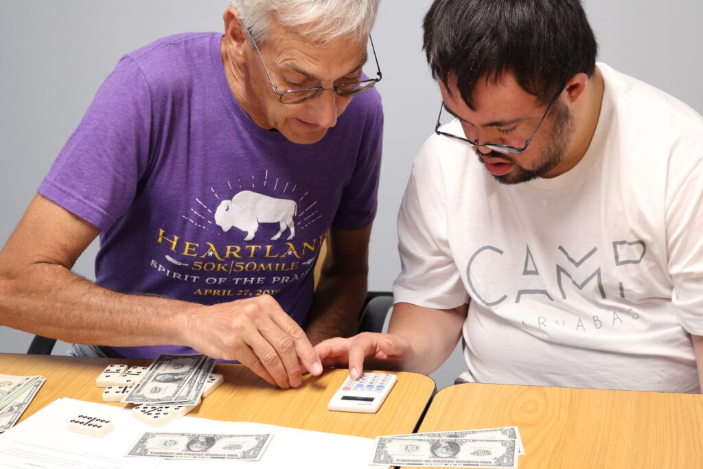 An older volunteer working with a student on money calculations.