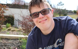 Male student outside, wearing sunglasses, and a blue tee shirt.
