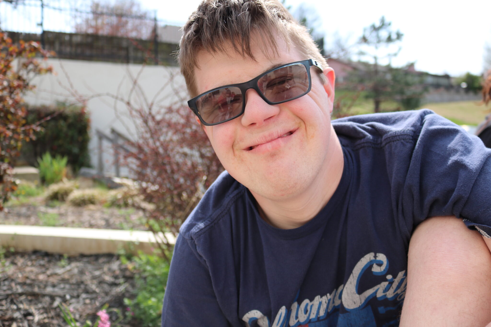 Male student outside, wearing sunglasses, and a blue tee shirt.