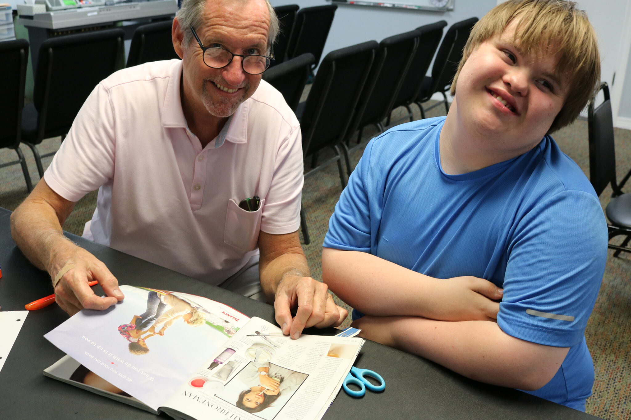 An older volunteer with a male student, looking through a magazine together.