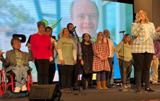 A group of Pathways students on a stage with a Monique, Executive Director, addressing the crowd.