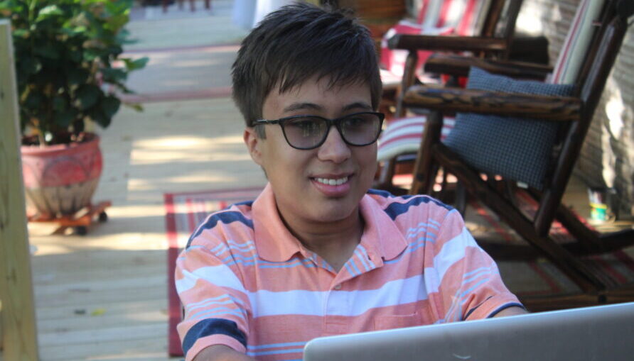 Photo of a Pathways student with glasses on, sitting outside on a computer for a virtual class.