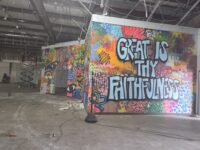 An image showing a wall with graffiti style are with words that say "Great is thy Faithfulness" and debrief surround it on the floor. 