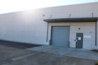 A photo of an exterior wall with a big metal door and a smaller door. 