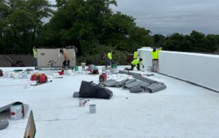 An image of the roof of a building with many construction workers in bright yellow working.