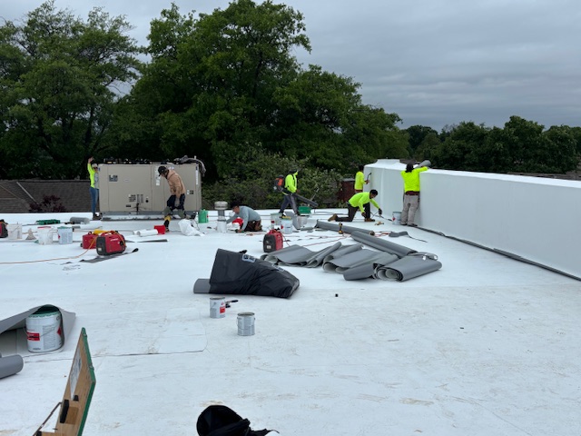 An image of the roof of a building with many construction workers in bright yellow working.