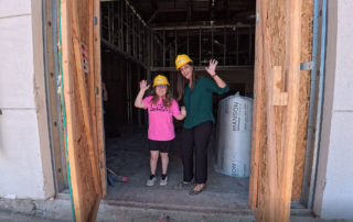 Student Emma Kindle and Erika Reeves, Development Director standing in the doorway of a construction site wearing hard hats.