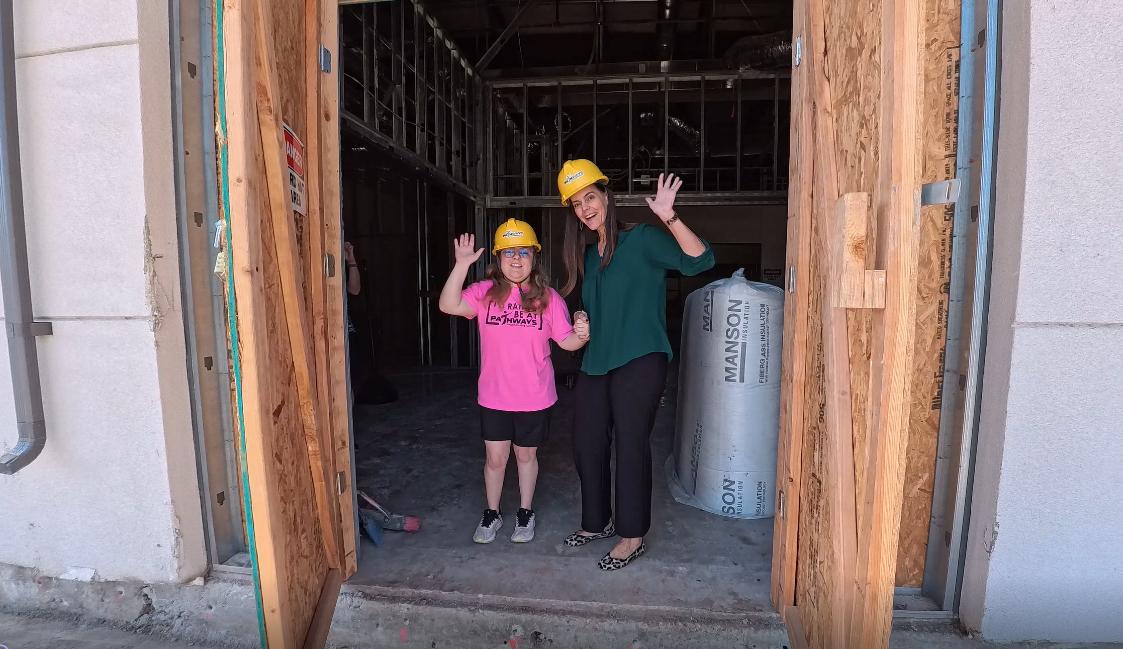 Student Emma Kindle and Erika Reeves, Development Director standing in the doorway of a construction site wearing hard hats.